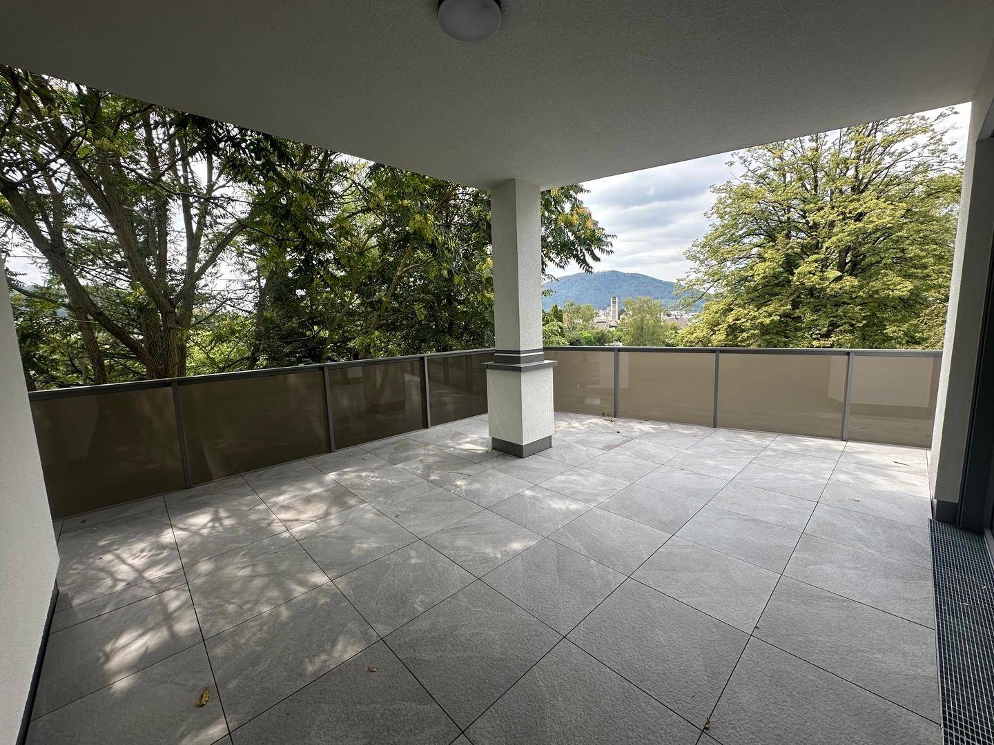 Geräumige, geflieste Terrasse mit Säule und weitem Blick auf die grüne Umgebung und Berge.