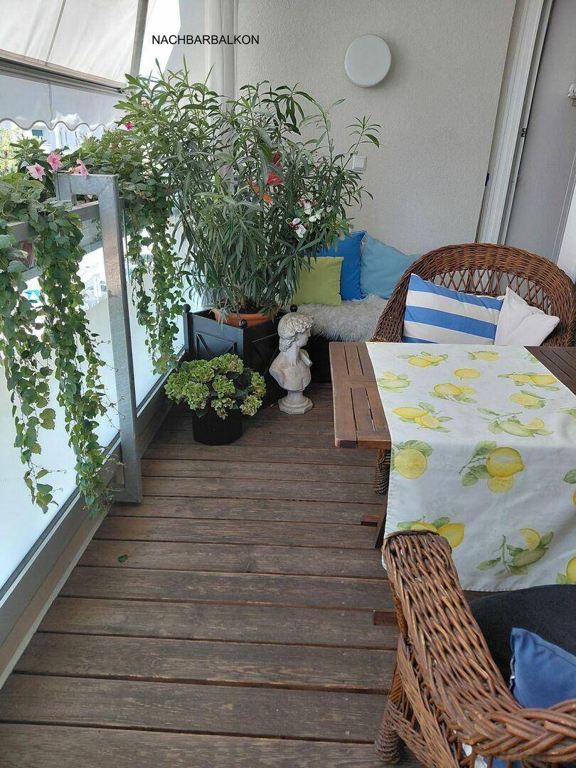 Gemütlicher Balkon mit Holzfußboden, vielen Pflanzen, Korbmöbeln und einem Tisch mit Zitronenmuster.