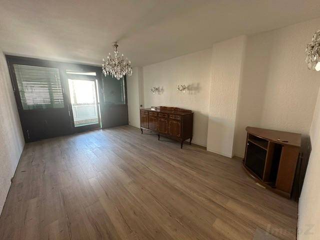 Geräumiges Wohnzimmer mit Laminatboden, Kronleuchter und Zugang zum Balkon.