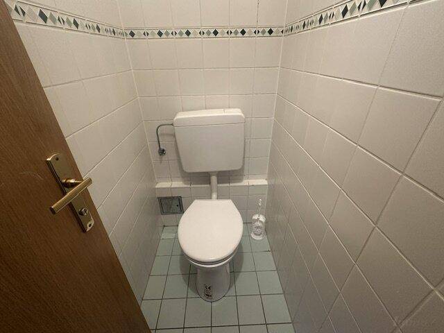 Kleines separates WC mit weiß gefliesten Wänden und Toilette.