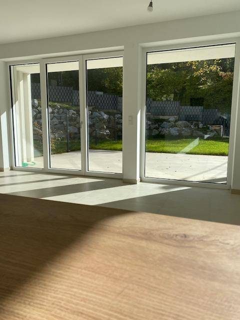 Heller Wohnraum mit großen Fenstern und Holzboden, bietet Zugang zur Terrasse.
