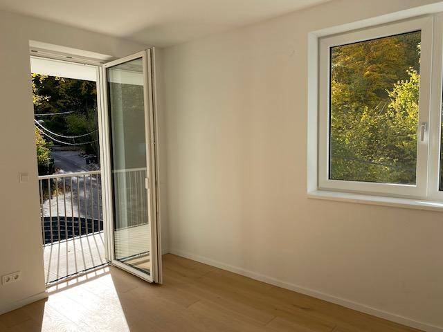 Heller Raum mit Holzboden und Zugang zu einem Balkon mit Blick ins Grüne.