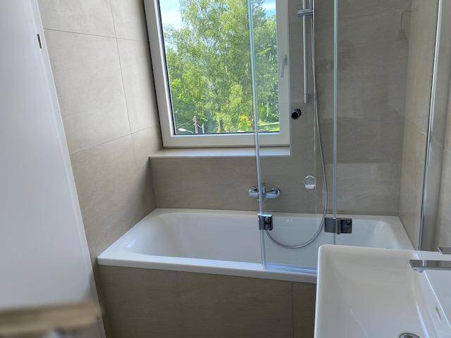Modernes Badezimmer mit Badewanne, Duschabtrennung und Fenster.