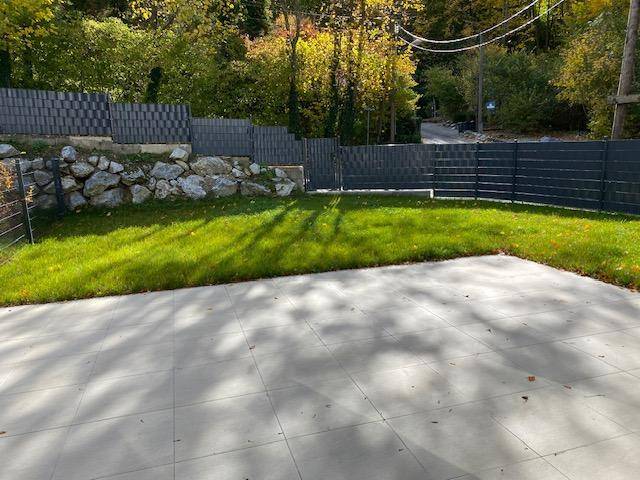 Sonniger Gartenbereich mit gepflegtem Rasen und gefliester Terrasse.