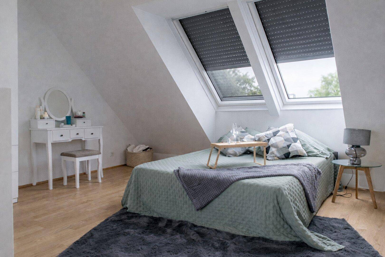 Schlafzimmer im Dachgeschoss mit schrägen Wänden, Dachfenstern und einem Schminktisch.