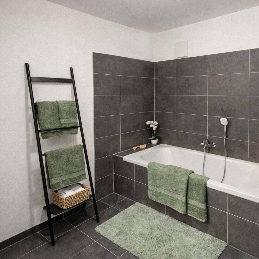 Badezimmer mit Badewanne, dunklen Wandfliesen und einem Handtuchhalter in Leiterform.