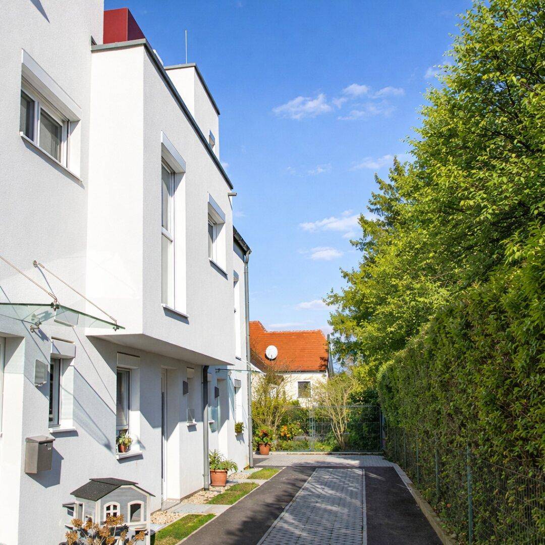 Seitenansicht der modernen Reihenhäuser mit Zufahrt und grüner Hecke.