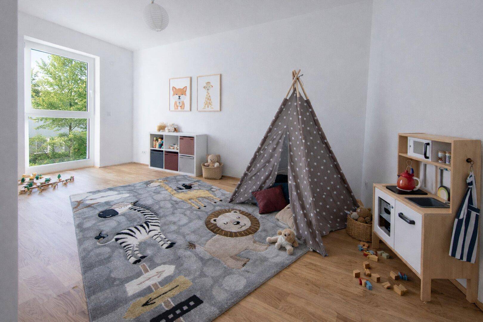 Helles Kinderzimmer mit Holzboden, Spielteppich und großem Fenster.