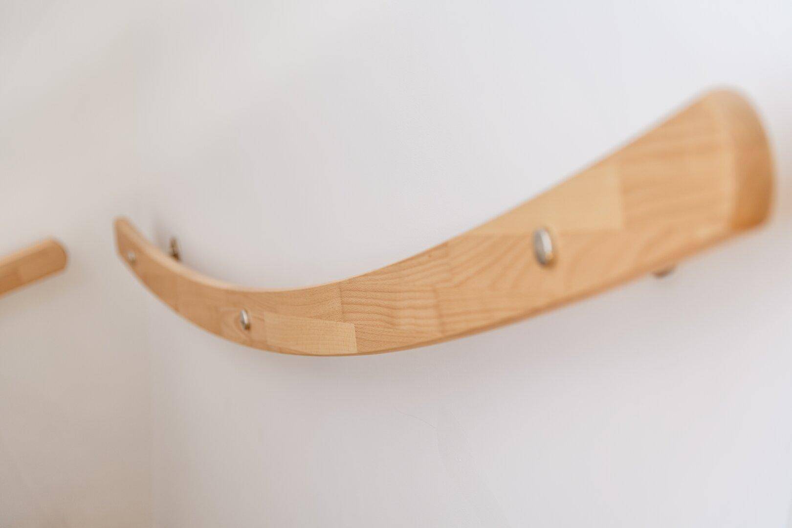 Detailaufnahme eines eleganten, geschwungenen Holzhandlaufs an einer weißen Wand.