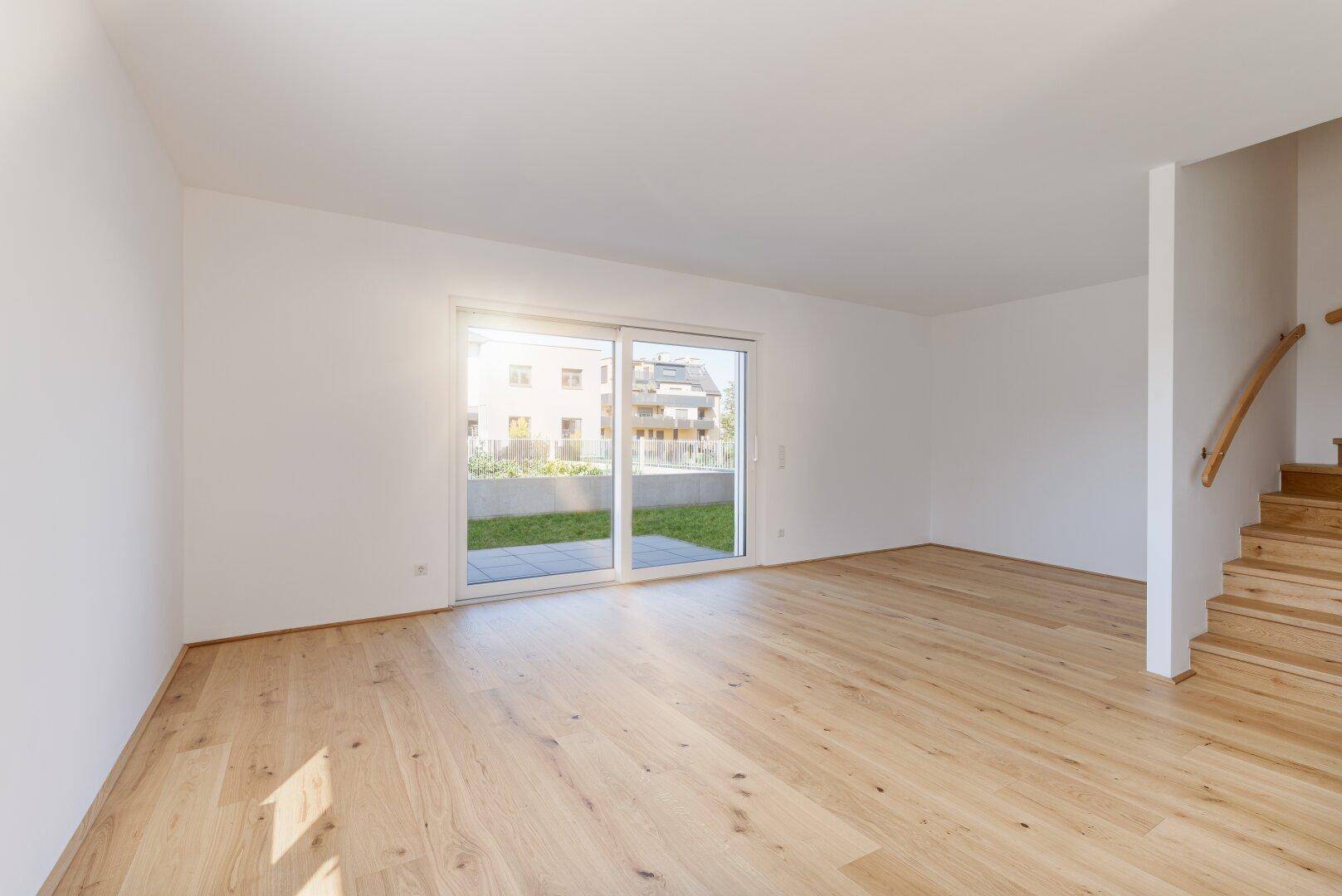 Heller, leerer Wohnraum mit Holzboden, großen Schiebetüren und Zugang zum Garten.