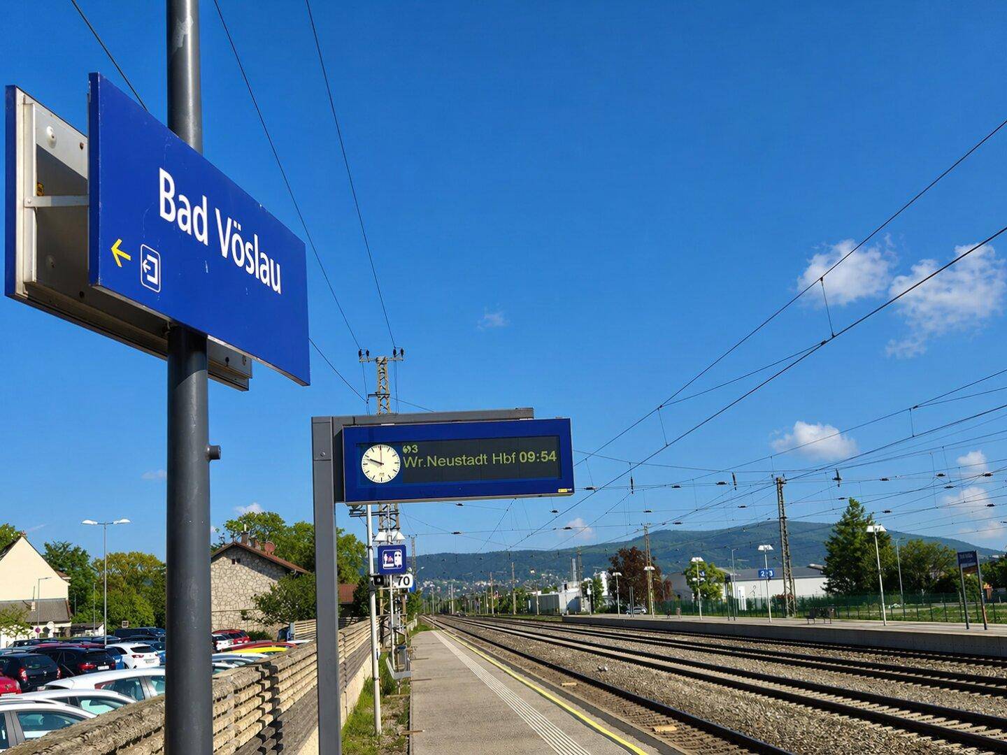 Bahnhof Bad Vöslau mit Gleisen, Bahnsteig und Blick auf die umliegende Landschaft.