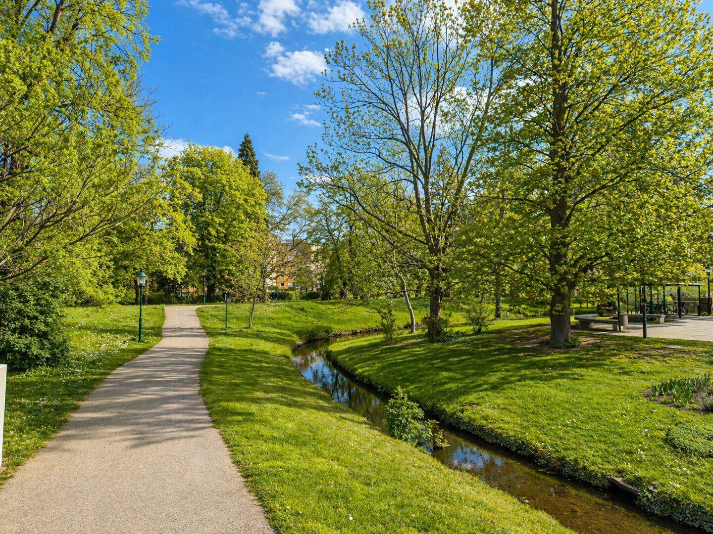 Idyllischer Park mit Spazierwegen, einem kleinen Bach und üppigem Grün.