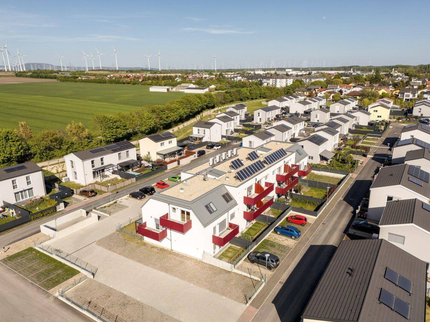 Luftaufnahme einer modernen Wohnsiedlung mit vielen Neubauten und Windrädern am Horizont.