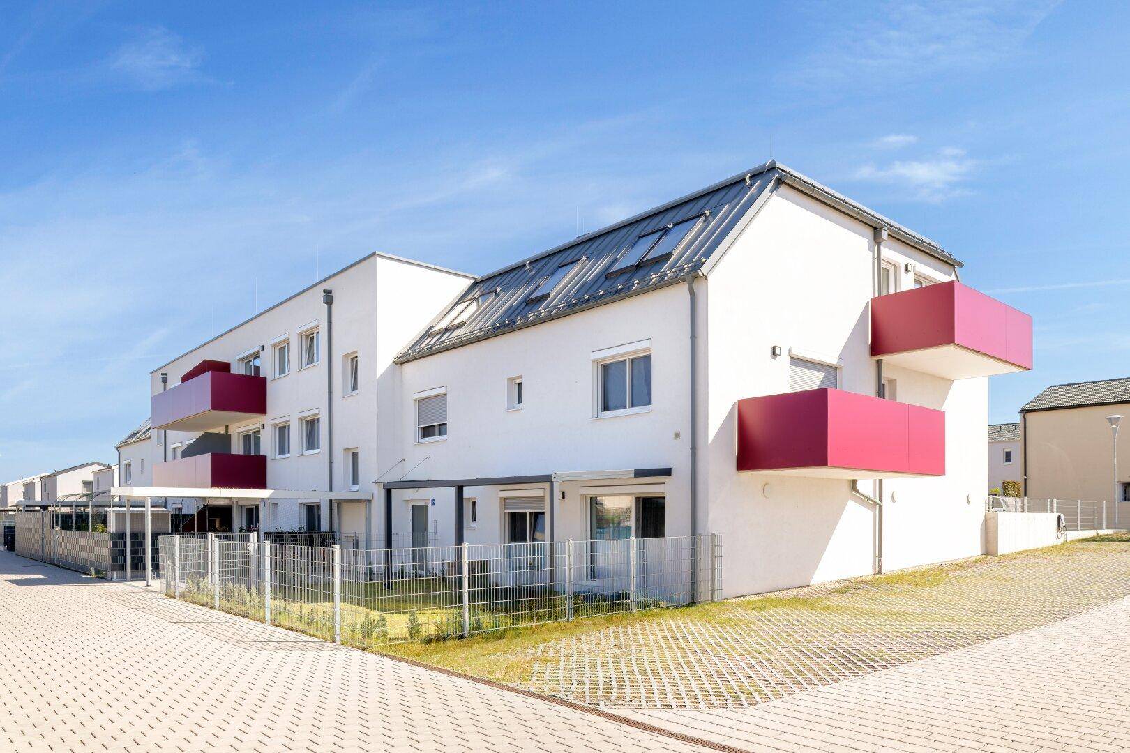 Moderne Wohnanlage mit weißer Fassade und auffälligen roten Balkonen unter blauem Himmel.