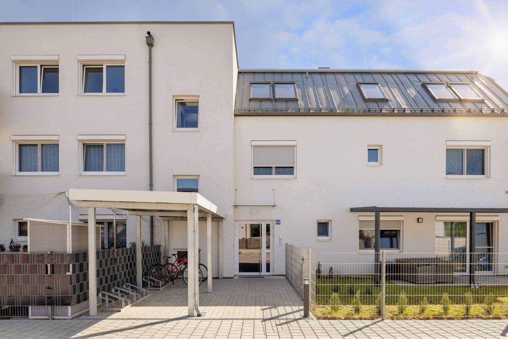 Eingangsbereich eines modernen Mehrfamilienhauses mit Carport und Fahrradabstellmöglichkeiten.