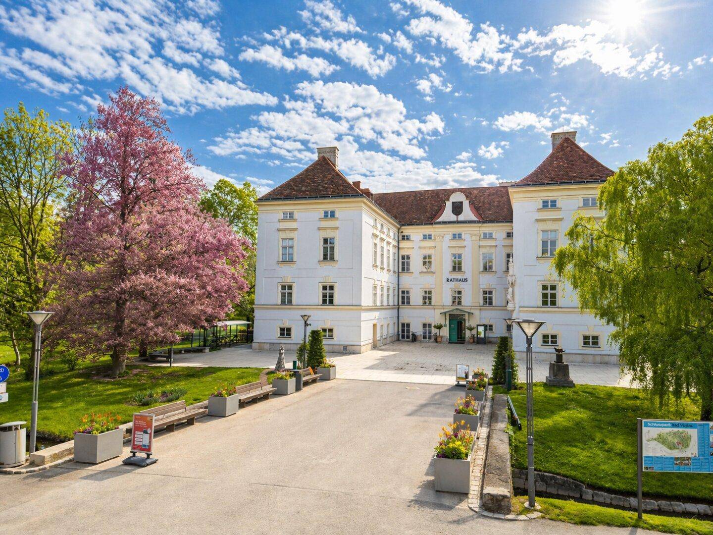 Elegantes weißes Rathausgebäude mit klassischer Architektur, umgeben von blühenden Bäumen und Grünflächen.