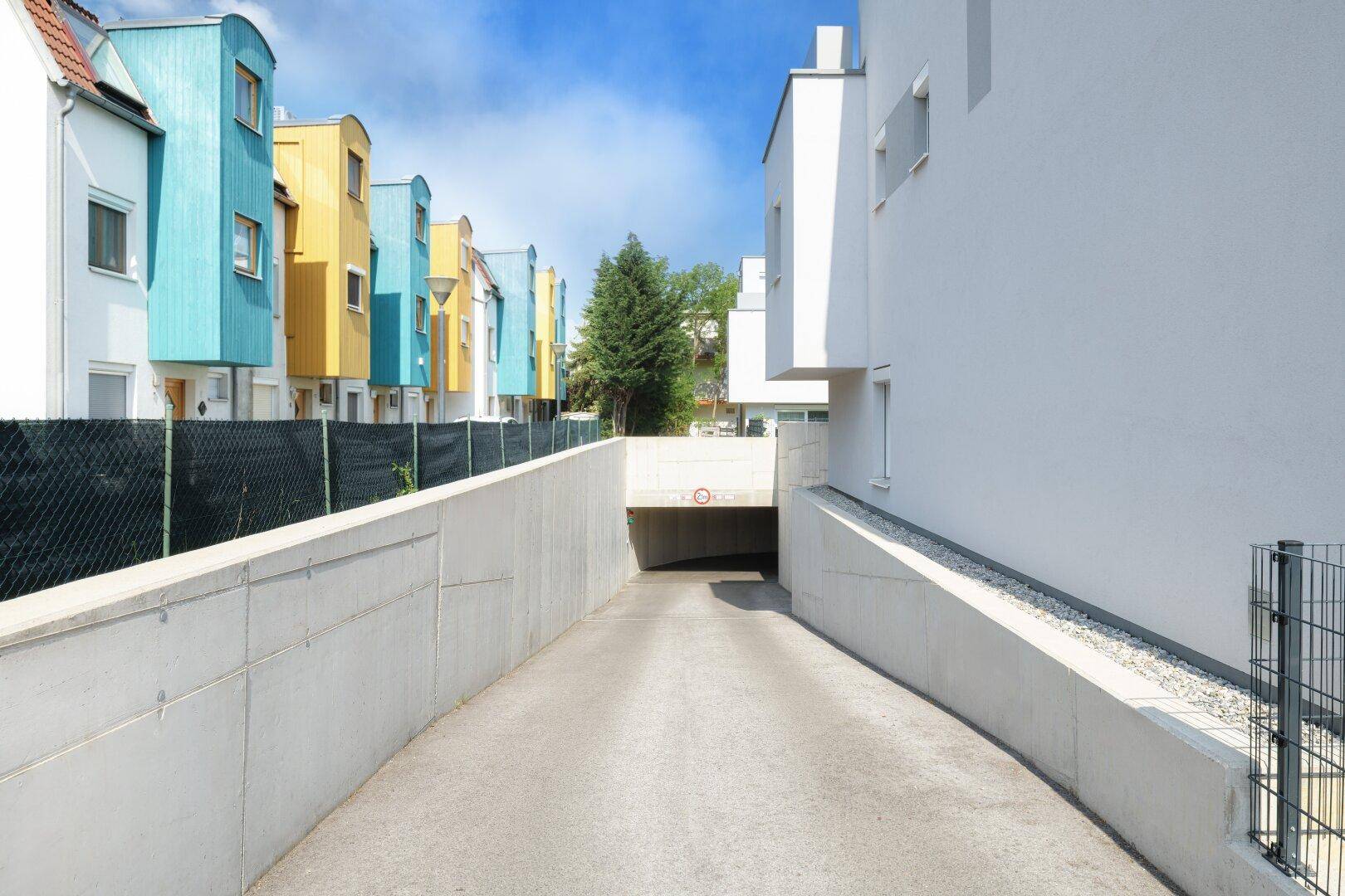 Zufahrt zu einer Tiefgarage zwischen modernen Gebäuden mit farbigen Fassaden.