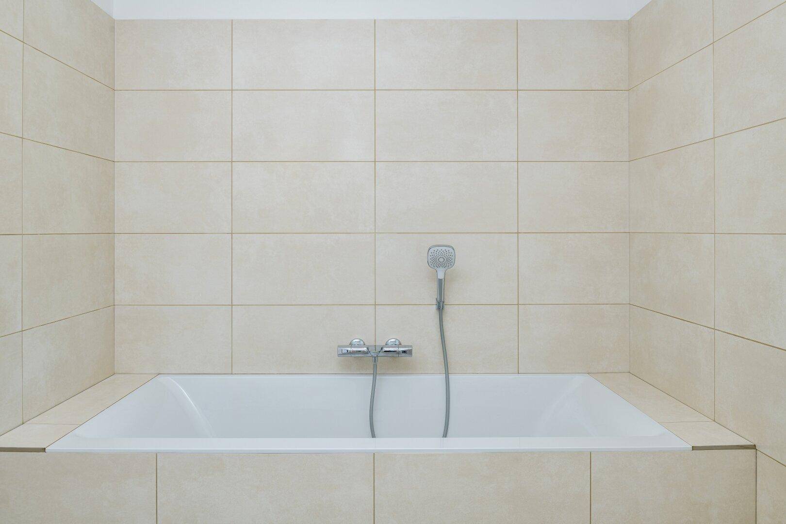 Eingebaute Badewanne mit beigefarbenen Fliesen und Duscharmatur.