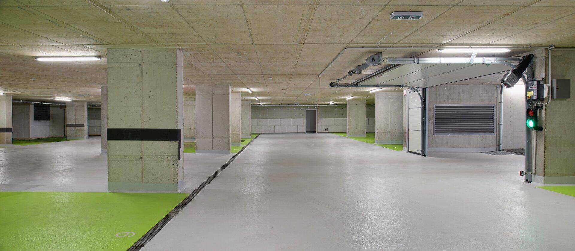 Geräumige Tiefgarage mit Betonpfeilern und hellgrauem Boden mit grünen Markierungen für Parkplätze.