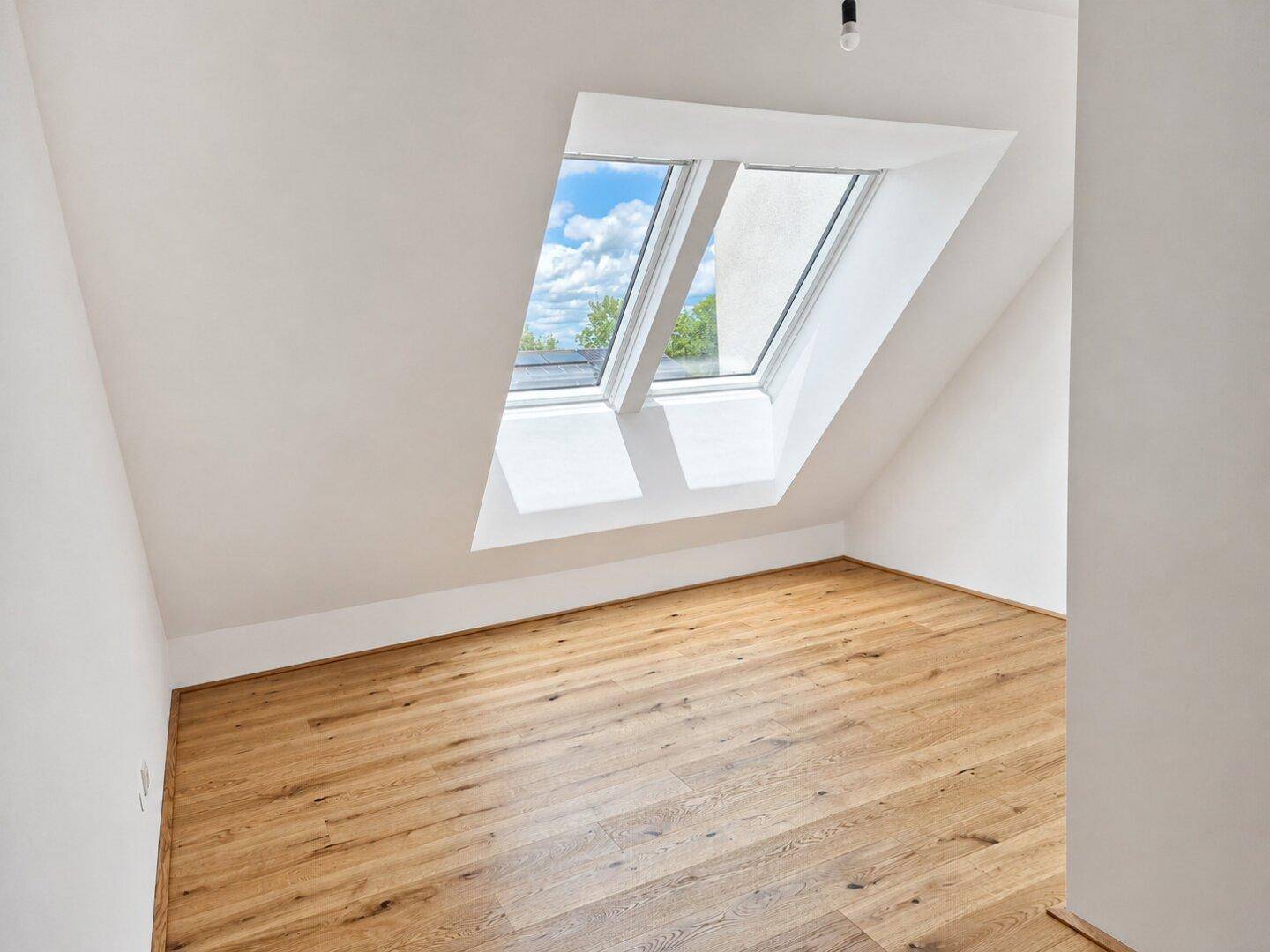 Helles Dachgeschosszimmer mit Holzboden und zwei großen Dachfenstern, ideal für ein Schlafzimmer.