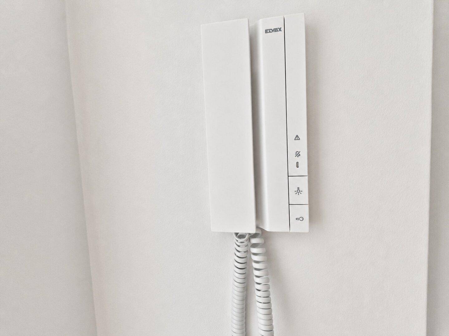 Nahaufnahme einer modernen weißen Gegensprechanlage an einer hellen Wand.