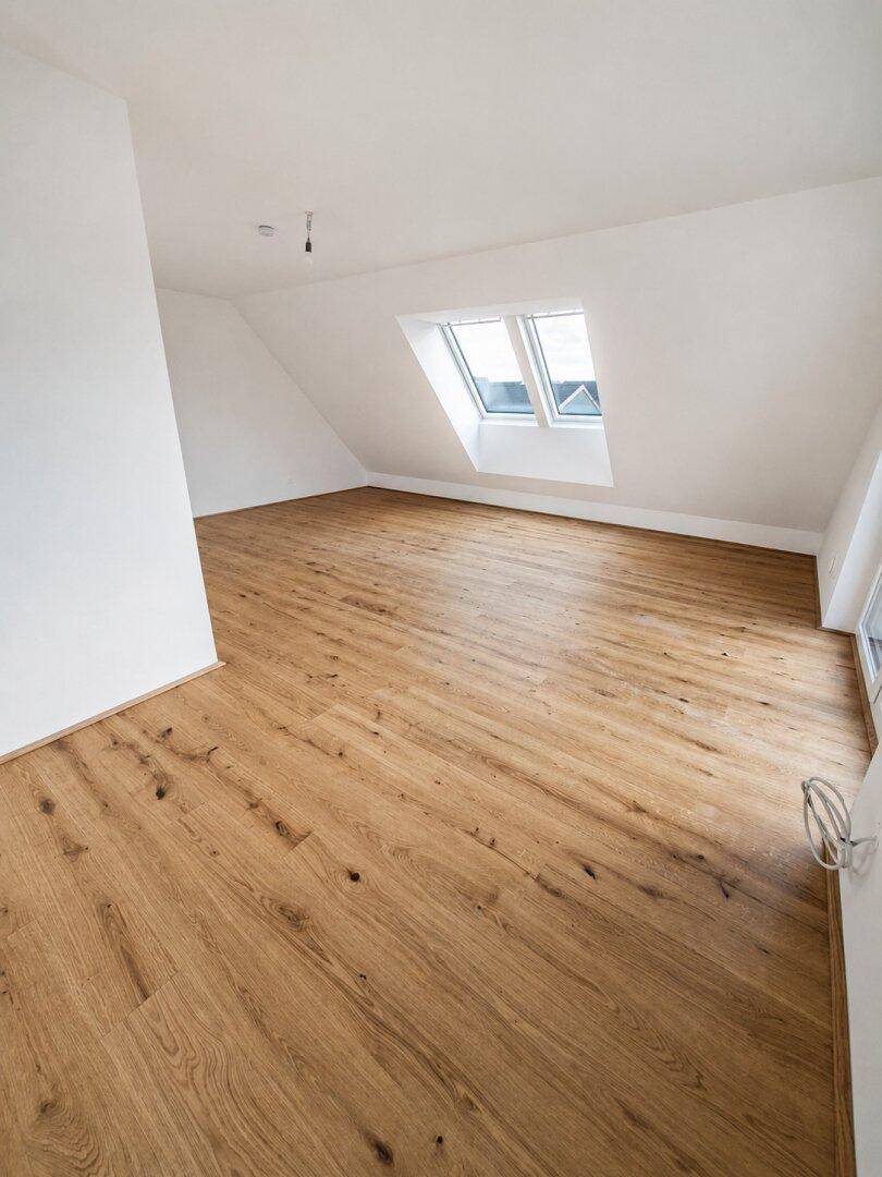 Geräumiges Dachgeschosszimmer mit hellem Holzboden und einem großen Dachfenster für viel Tageslicht.