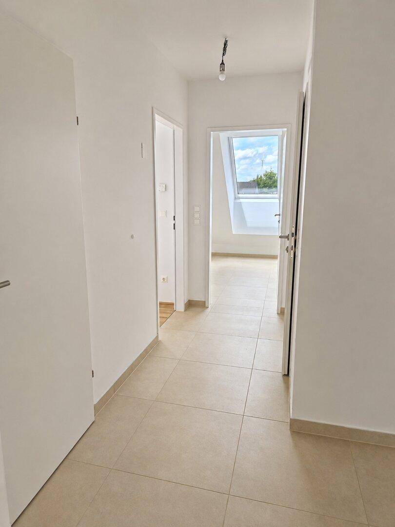 Heller Flur mit beigefarbenen Fliesen und Zugang zu verschiedenen Zimmern, inklusive Blick in ein Dachgeschosszimmer.