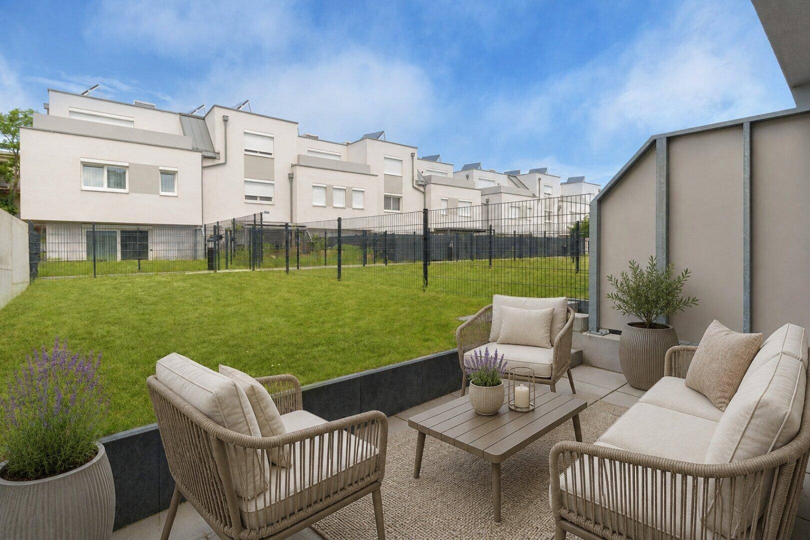 Moderne Terrasse mit bequemen Gartenmöbeln und Blick auf den Gemeinschaftsgarten und Reihenhäuser.