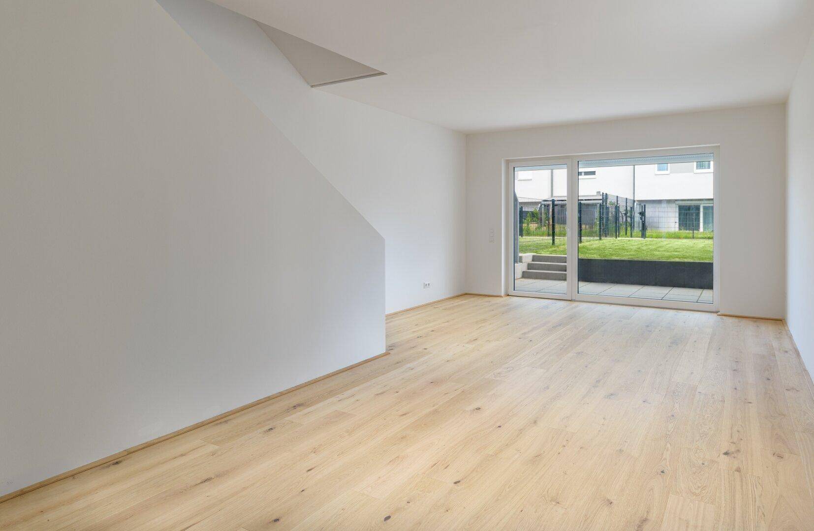Heller, leerer Raum mit Holzboden und Zugang zu einem kleinen Garten, ideal für individuelle Gestaltung.
