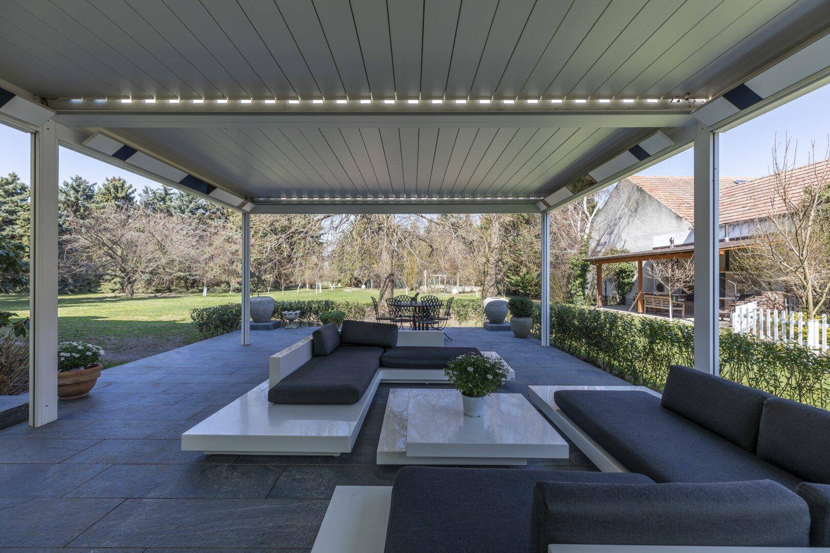 Große überdachte Terrasse mit modernen Lounge-Möbeln und Blick in den Garten.