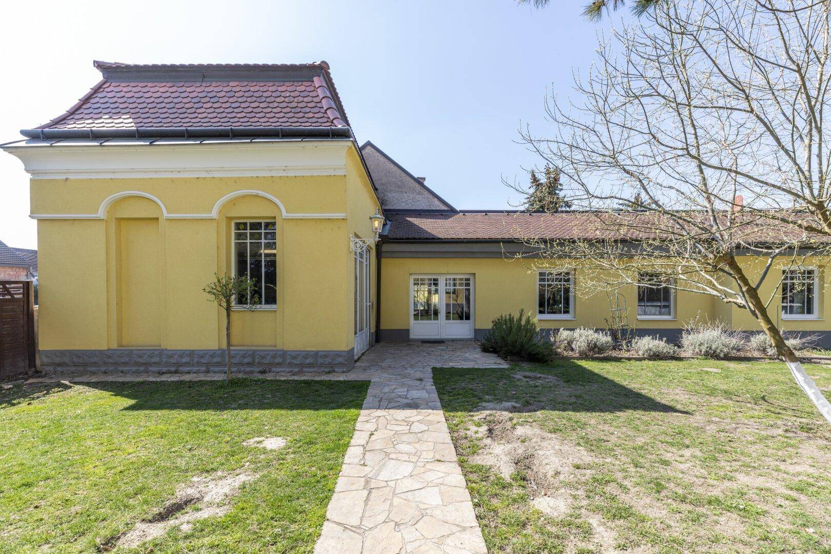Seitenansicht der gelben Villa mit Steinweg und gepflegtem Rasen.