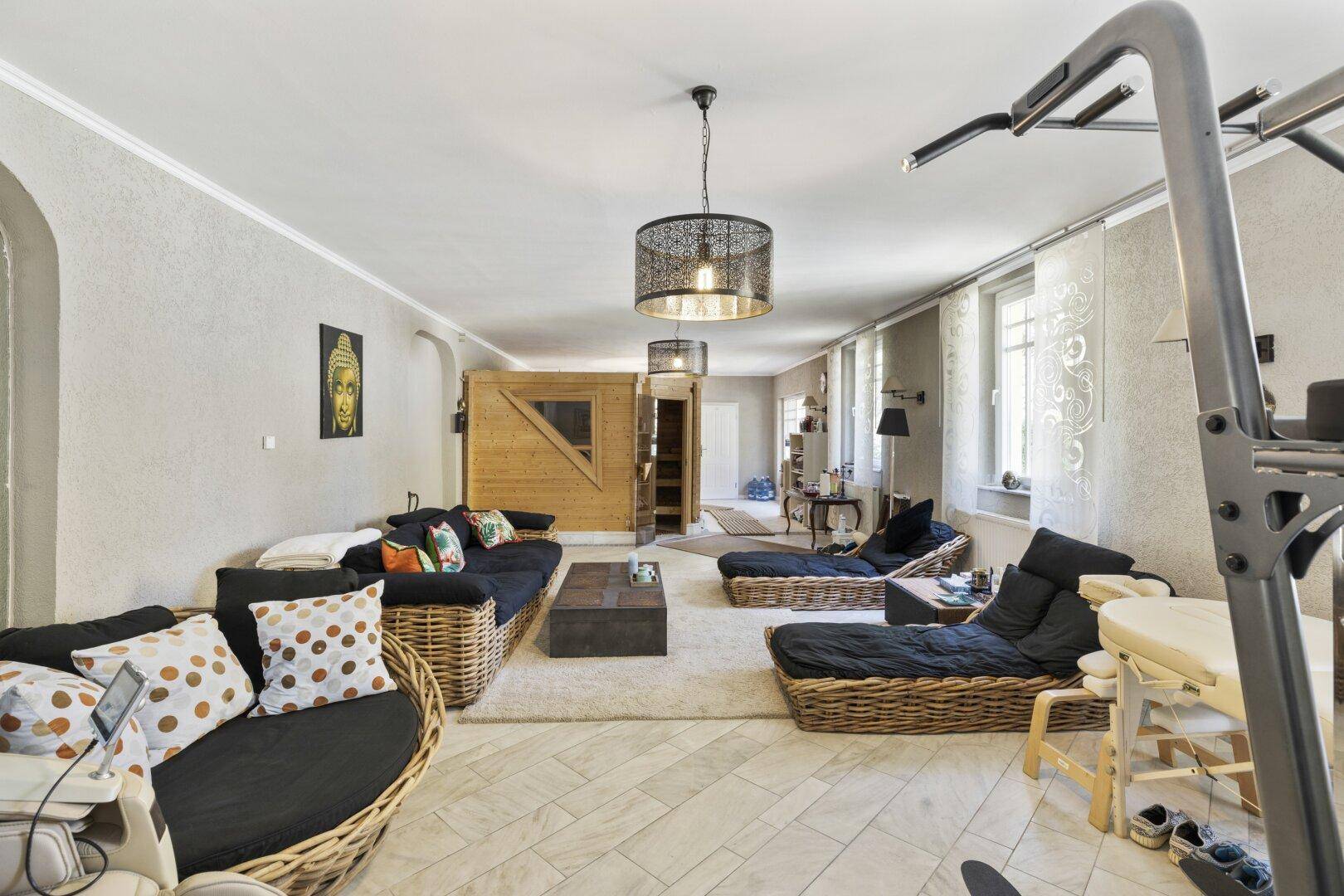 Großer Wohn- und Wellnessbereich mit Sauna, Lounge-Möbeln und Fitnessgeräten.