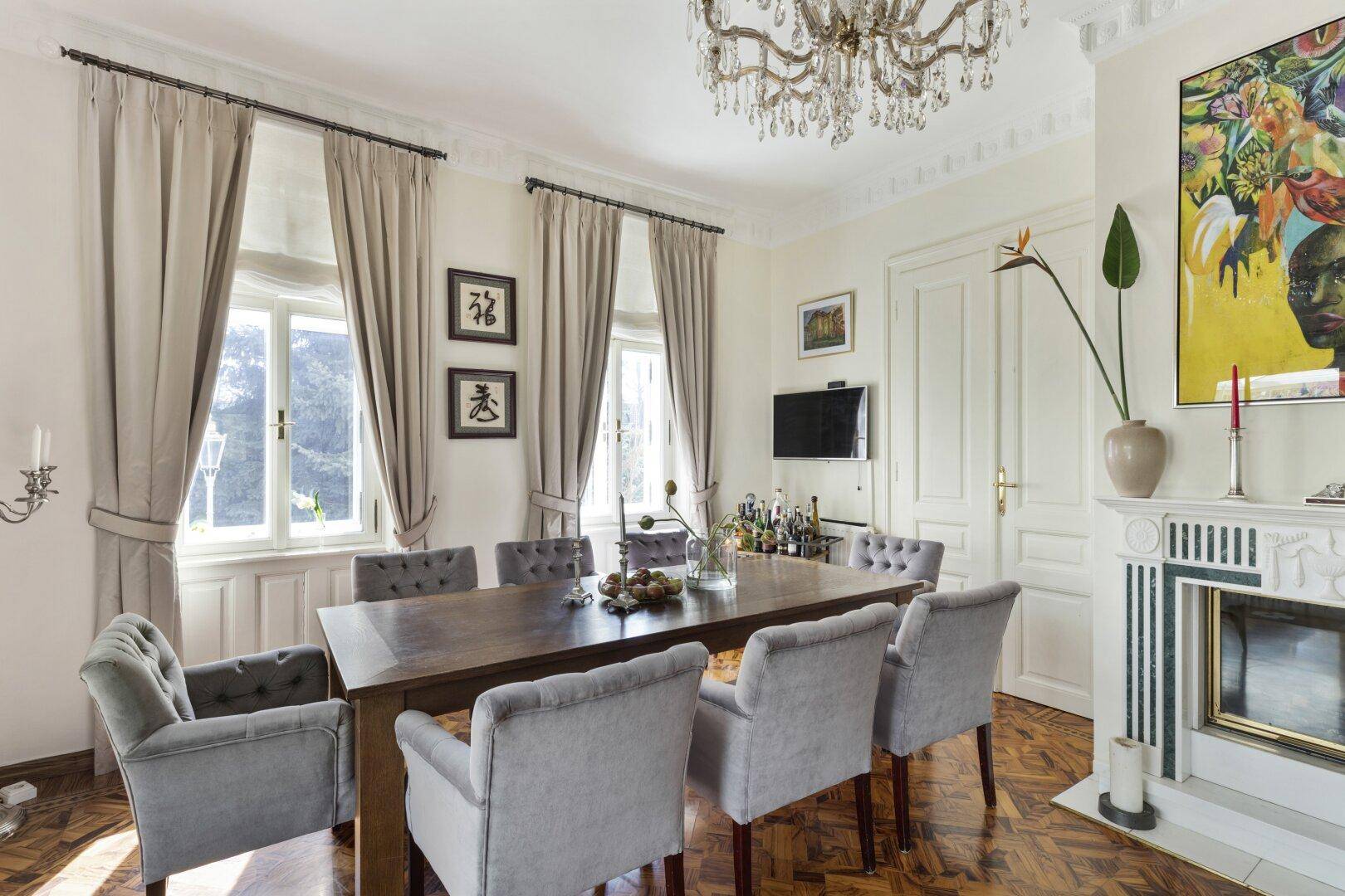 Elegantes Esszimmer mit Holztisch, Samtstühlen, Kronleuchter und Kamin.