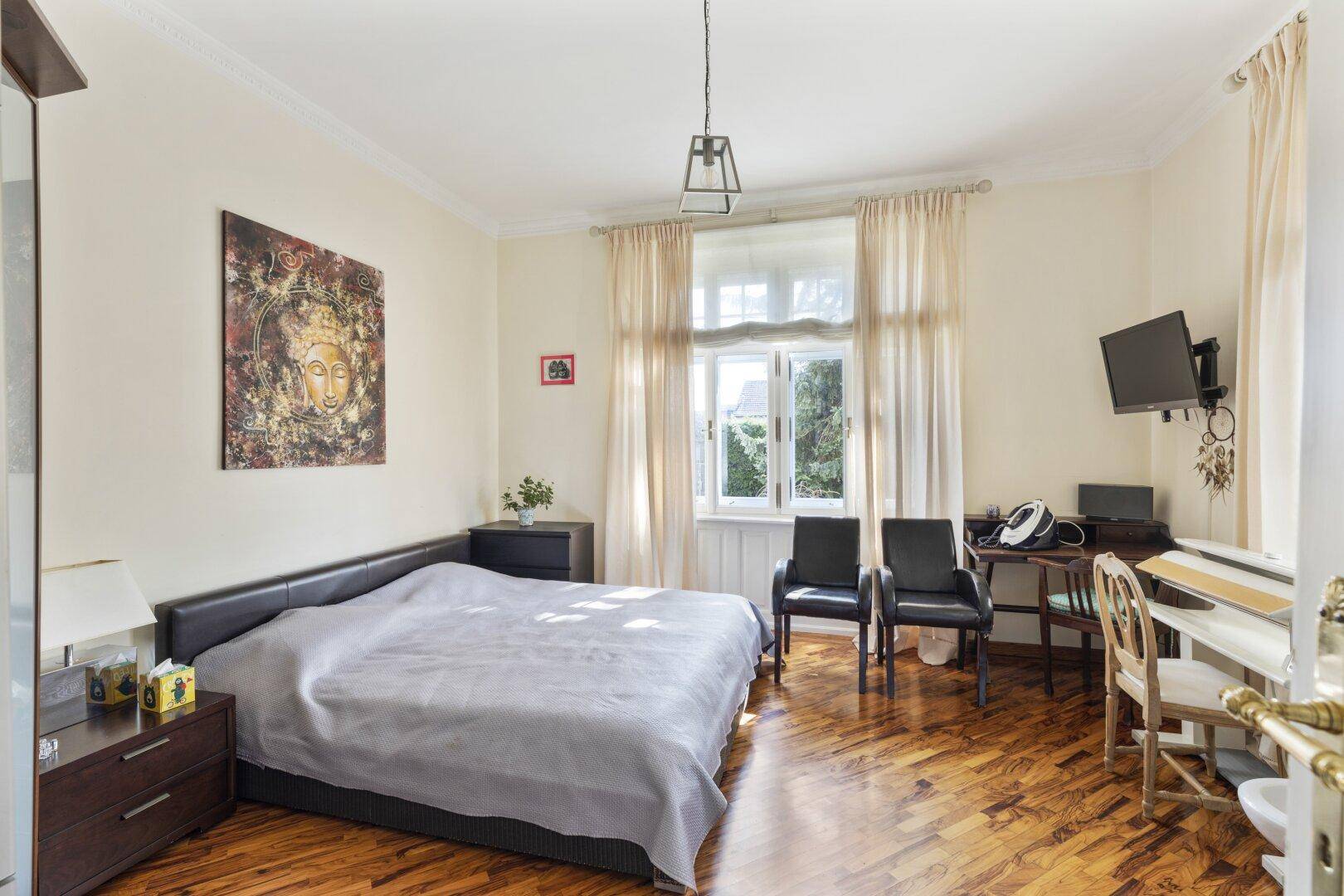 Helles Schlafzimmer mit Doppelbett, Holzboden, Schreibtisch und Blick ins Grüne.