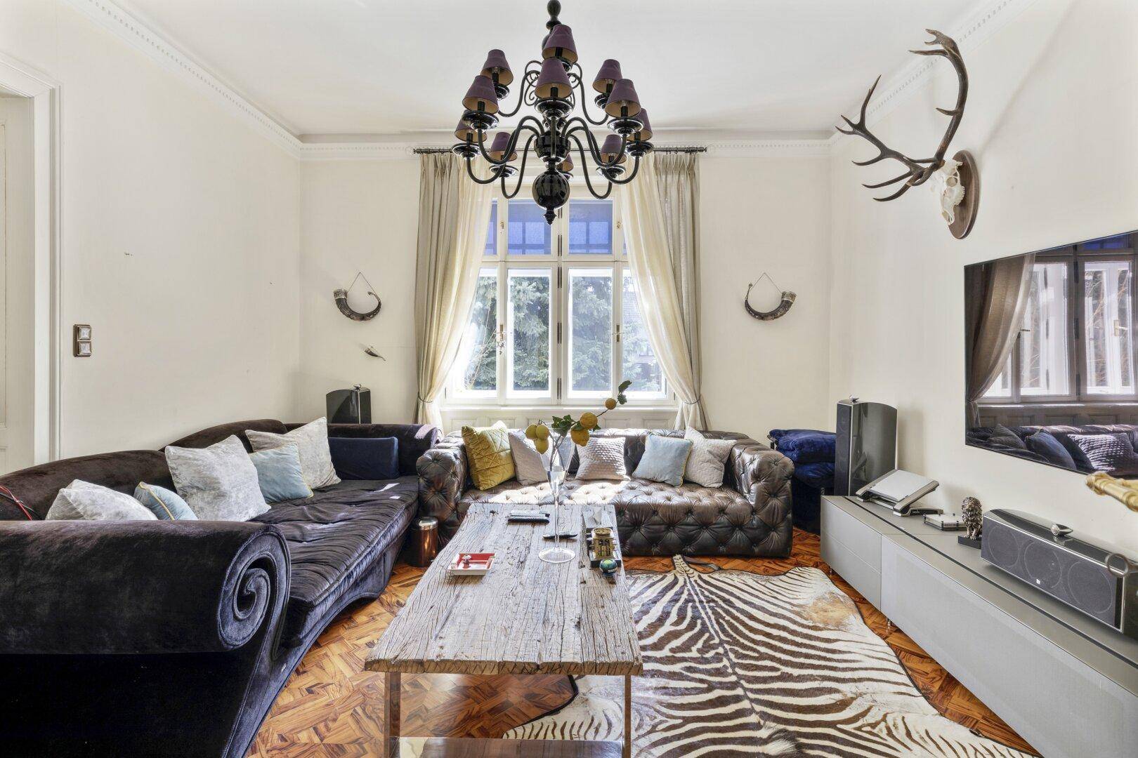 Gemütliches Wohnzimmer mit großer Couch, Holzboden, Kronleuchter und Hirschgeweih.