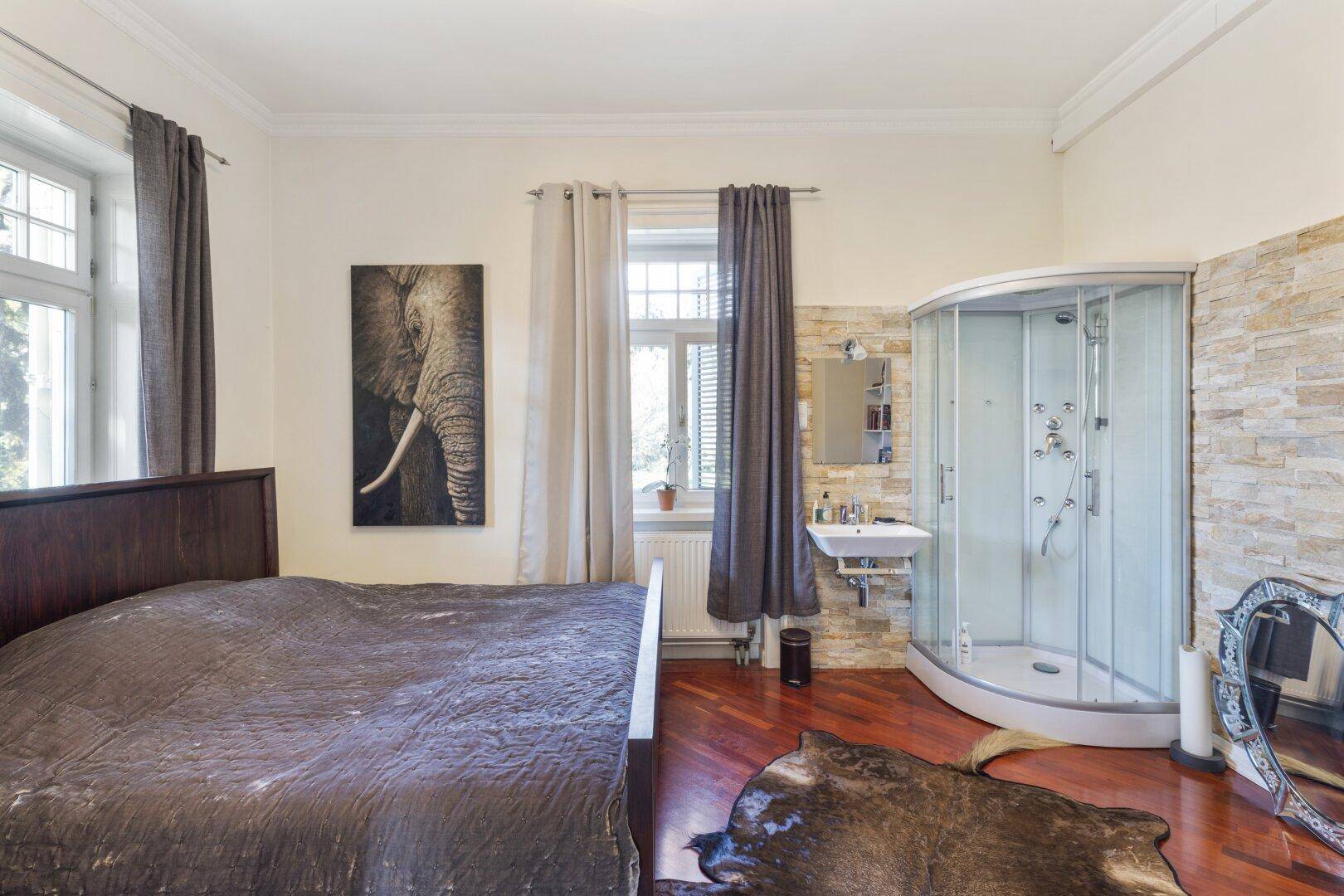 Schlafzimmer mit Holzbett, Parkettboden und integrierter Duschkabine.