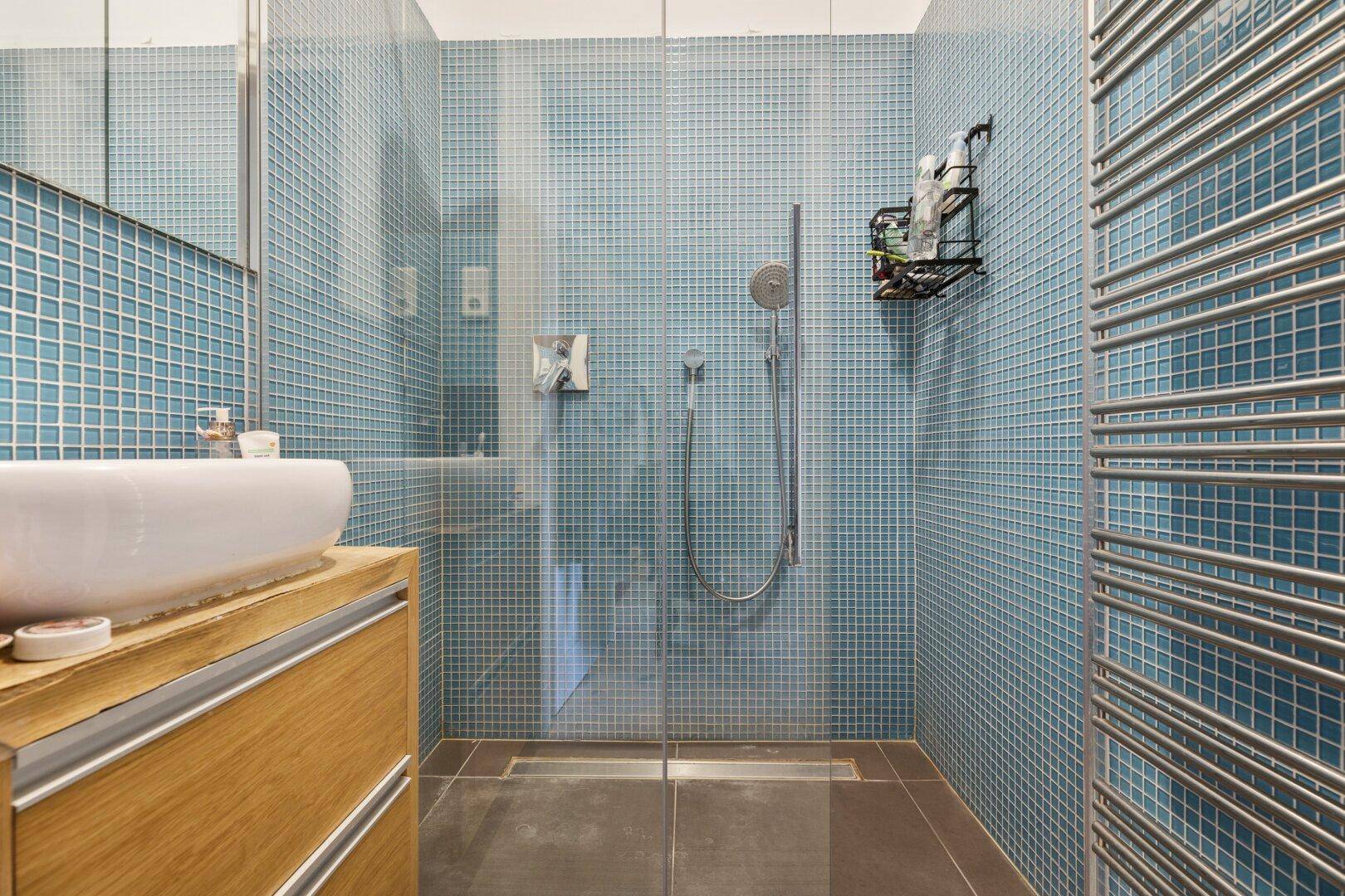 Modernes Badezimmer mit blauen Mosaikfliesen, ebenerdiger Dusche und Handtuchheizkörper.