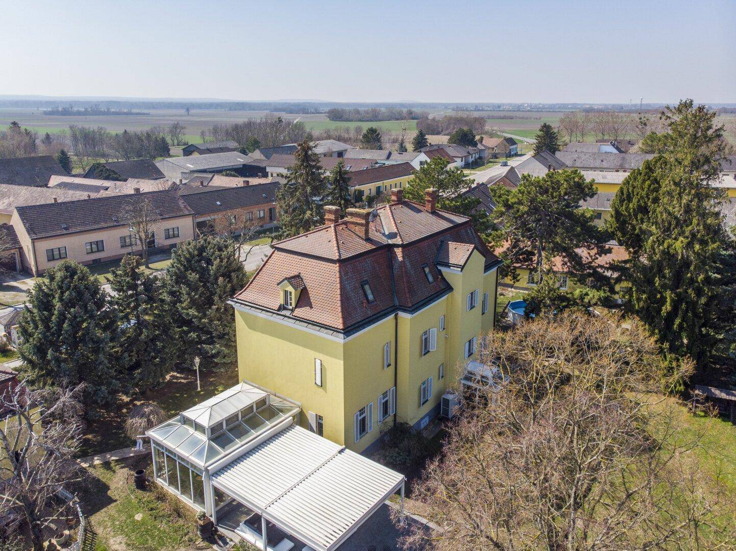 Luftbild der historischen Villa mit Wintergarten und Blick auf die umliegende Landschaft und das Dorf.