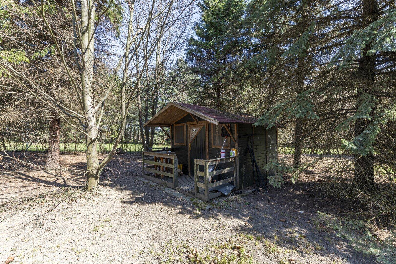 Kleiner Holzschuppen mit Vordach, eingebettet in eine bewaldete Umgebung auf dem Grundstück.