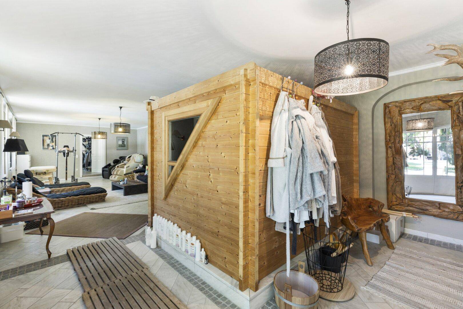 Integrierte Holzsauna in einem großzügigen Wellnessbereich mit Spiegel und Sitzgelegenheiten.