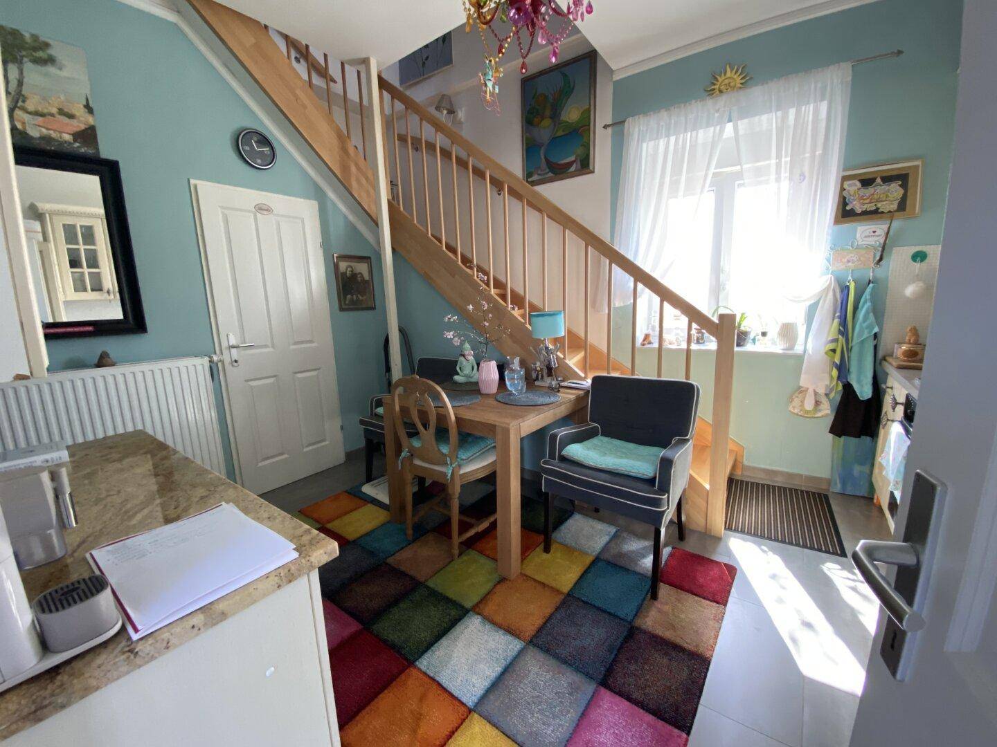 Bunte Küche mit Esstisch, Holztreppe und farbenfrohem Teppich.