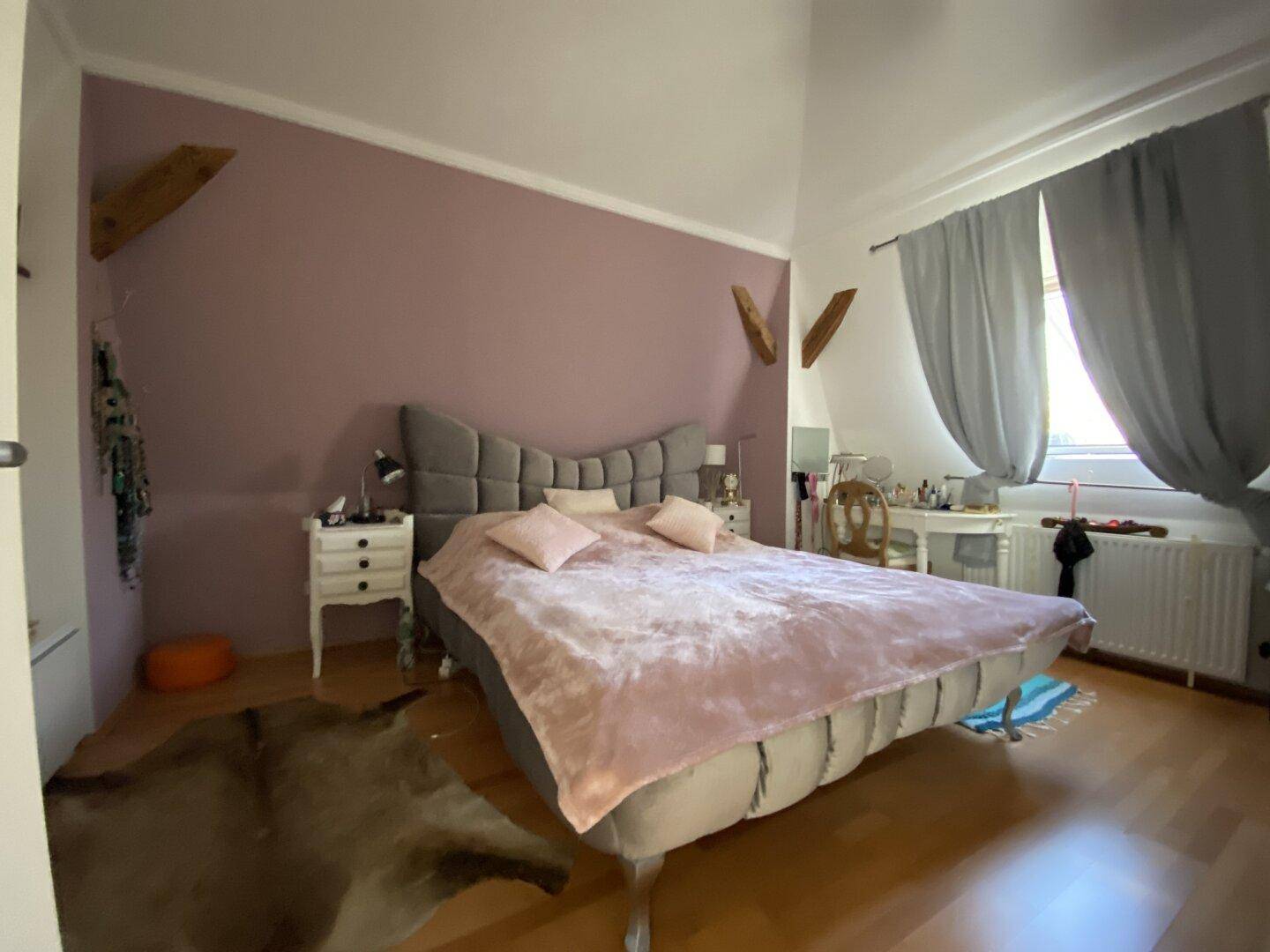 Gemütliches Schlafzimmer mit großem Bett, Holzboden und farbiger Akzentwand.