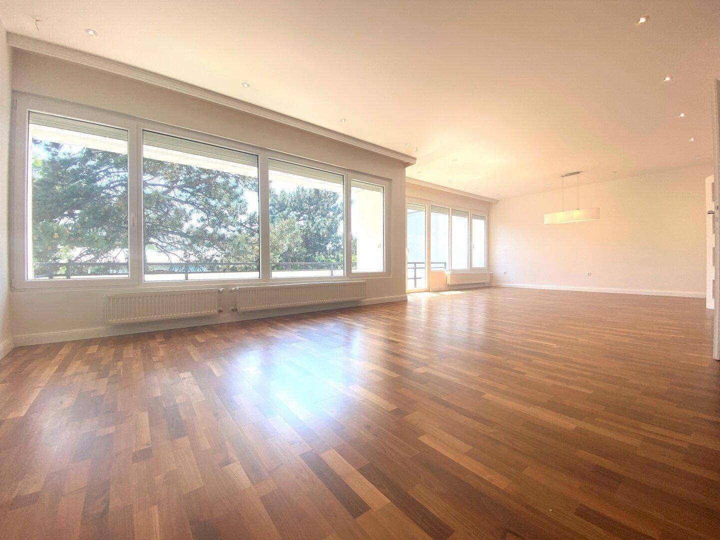 Helles Wohnzimmer mit durchgehendem Parkettboden und breiter Fensterfront mit Ausblick.