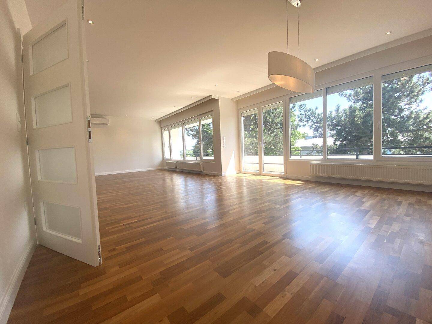 Weitläufiges Wohnzimmer mit Parkettboden und bodentiefen Fenstern, die viel Licht hereinlassen.