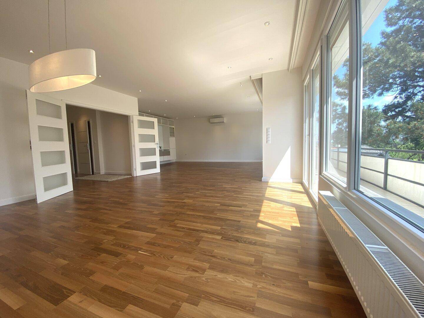 Geräumiges Wohnzimmer mit Holzparkettboden, großen Fenstern und viel Tageslicht.