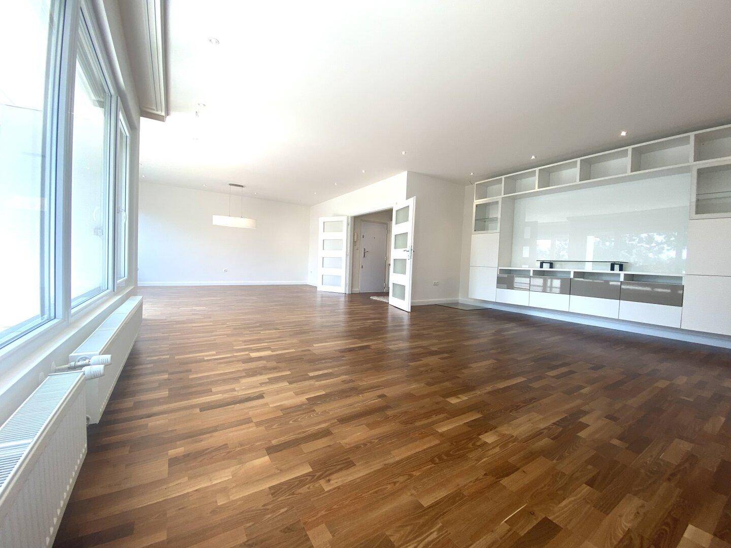 Großes Wohnzimmer mit Parkettboden und moderner, weißer Einbauschrankwand.