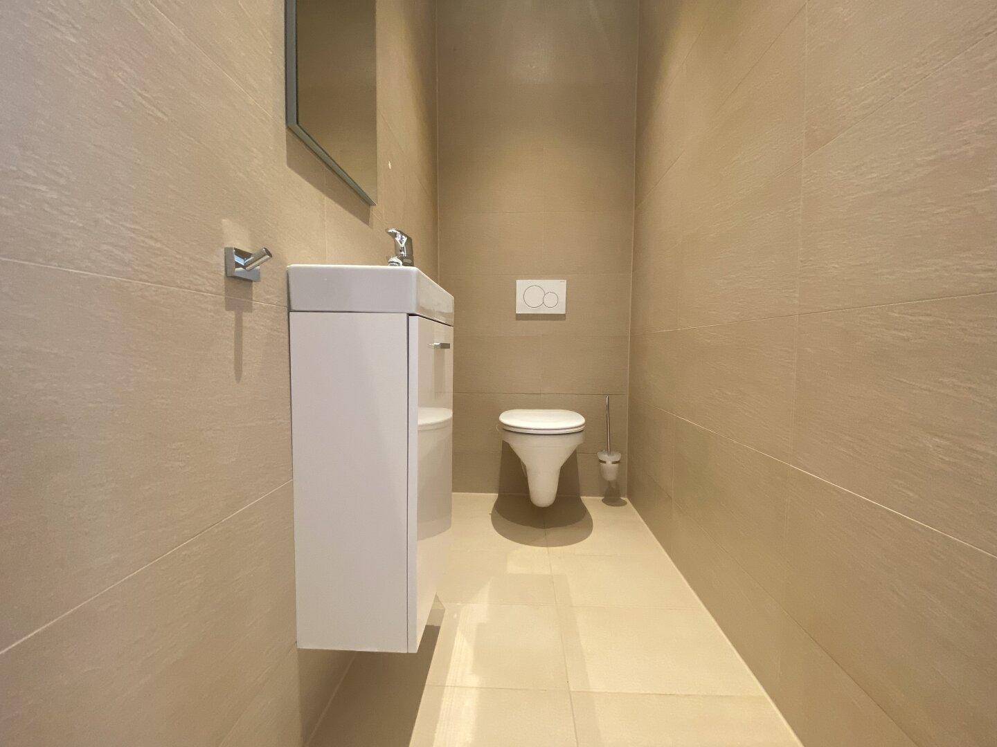 Modernes Gäste-WC mit wandhängendem WC, kleinem Waschbecken und beigefarbenen Fliesen.