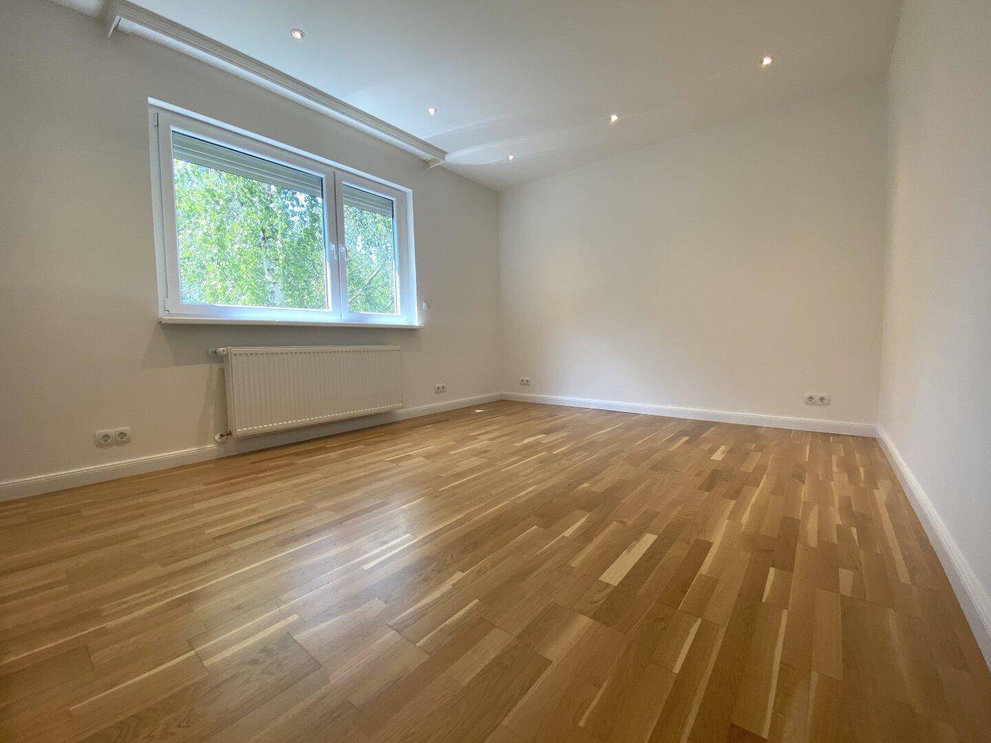 Helles Schlafzimmer mit Holzparkettboden und großem Fenster, bereit zur individuellen Gestaltung.
