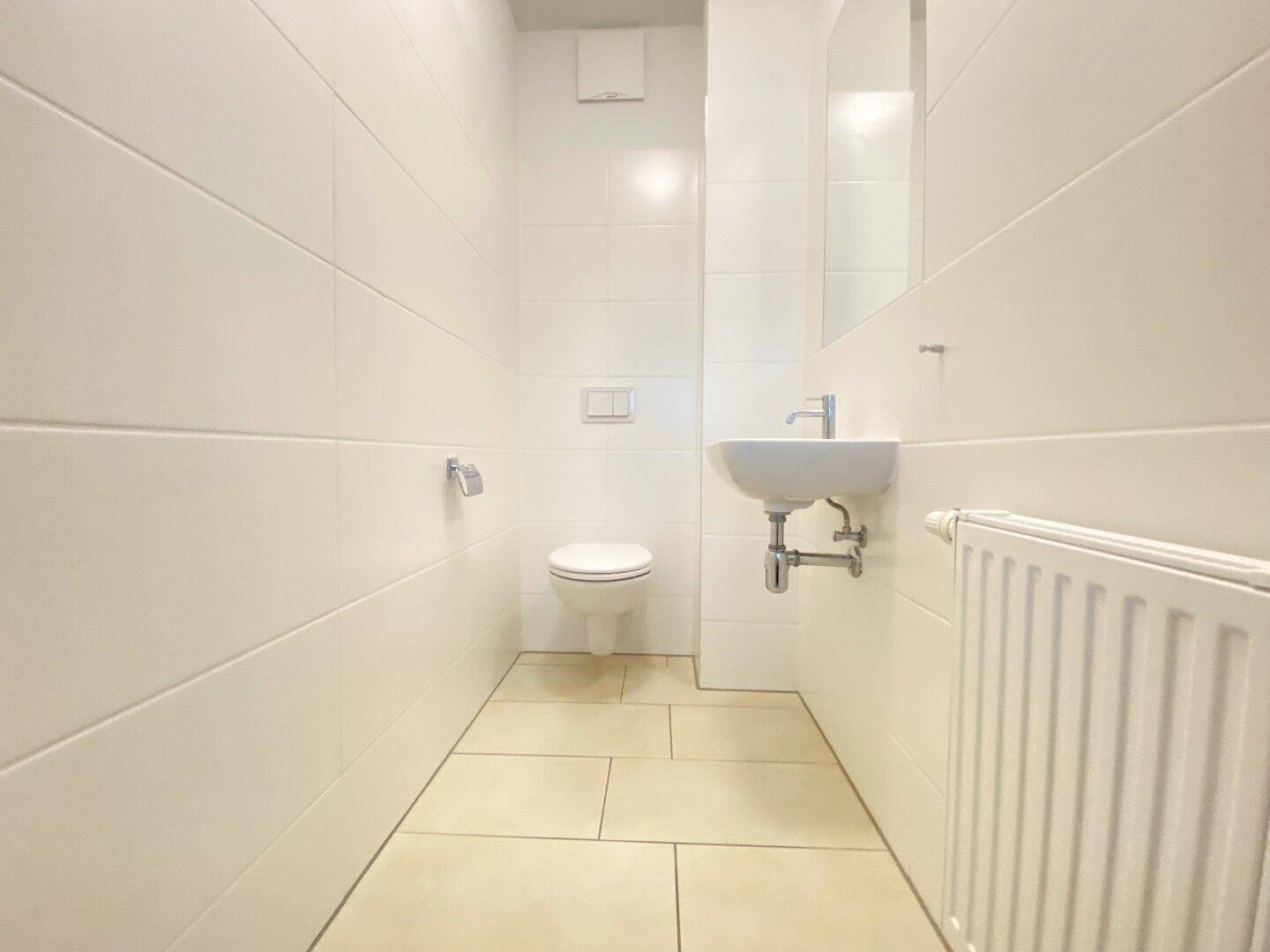 Modernes Gäste-WC mit wandhängender Toilette, kleinem Waschbecken und weißen Fliesen.