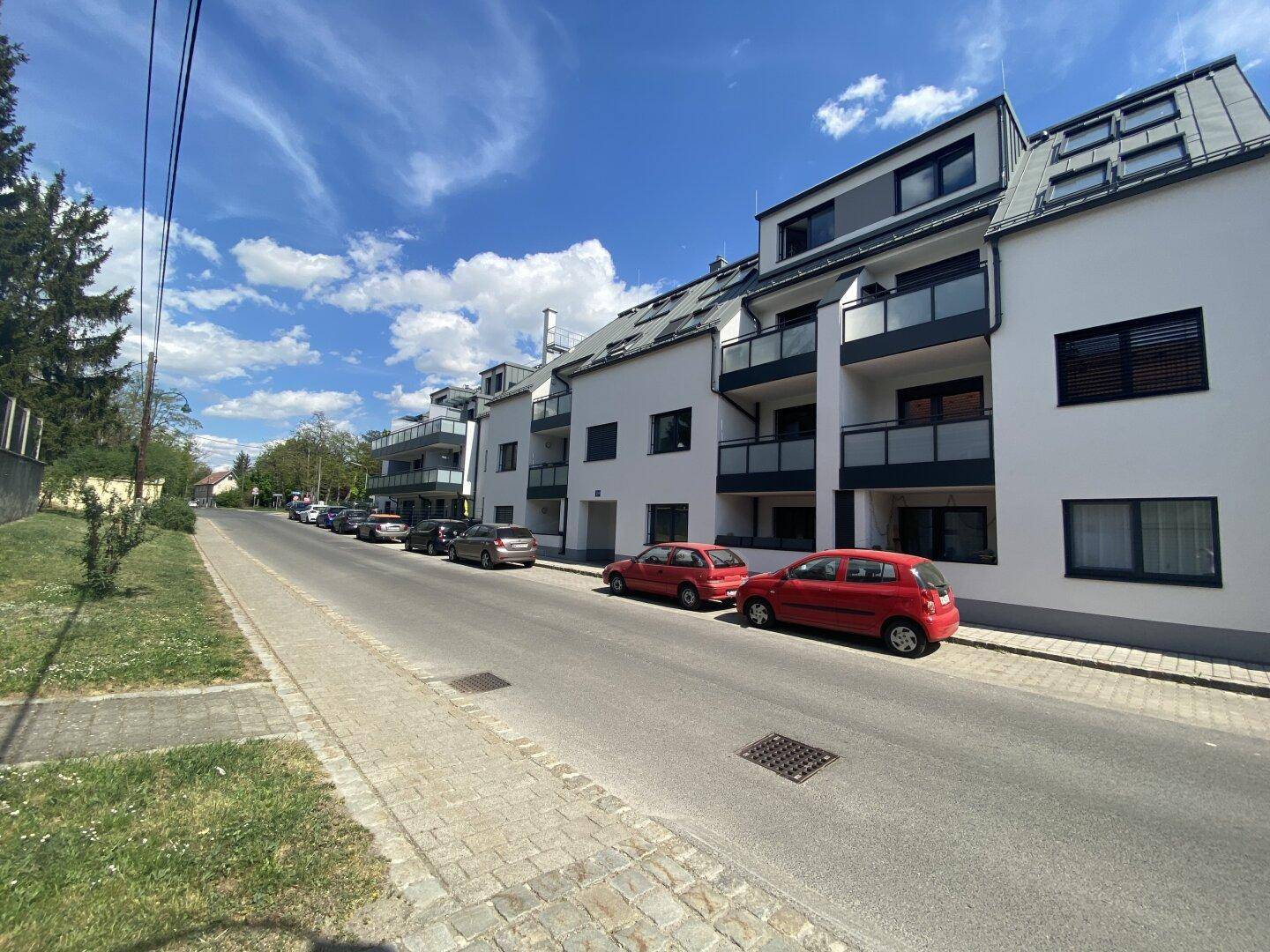 Moderne Wohnanlage mit mehreren Balkonen und großen Fenstern entlang einer Straße.